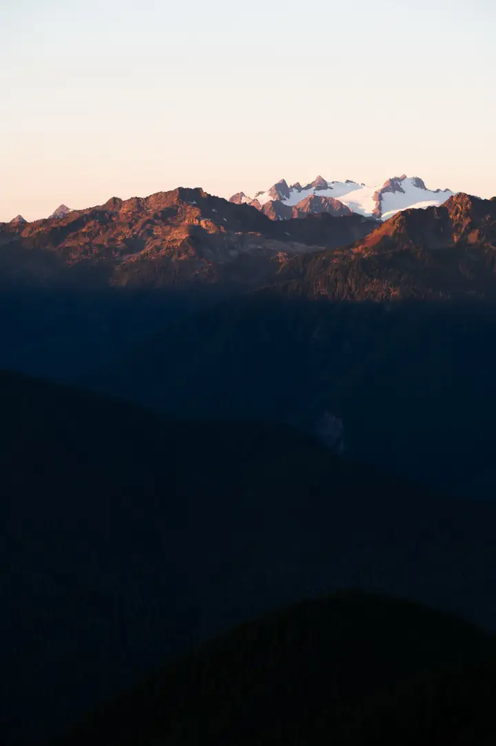 Ridges of the Cascade Range at dusk, snow on the far peaks, dark forested slopes in the foreground.